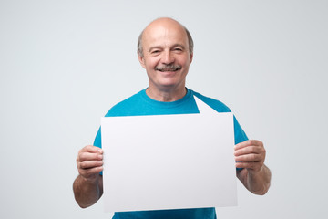 Senior hispanic man with mustache holds the white sign in a studio white background. look here, great offer