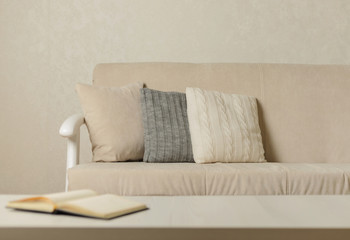 Autumn (winter) concept - coziness and warmth in the house. Beige sofa with plaid and pillows in the living room.