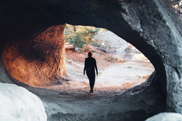 Silhouette of a girl exploring a mountain rock stone cave in moody sunset light. Sandstone rock...