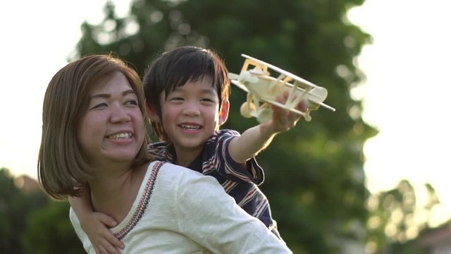 Cute Asian mother and son playing wooden airplane together in the park outdoors slow motion 