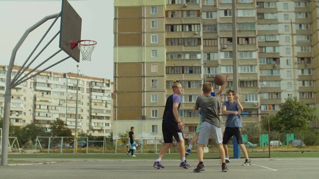 Active teenage friends playing two on two streetball game on outdoor basketball court. Young basketball player scoring field goal with layup shot after assist from his teammate during game outdoors.