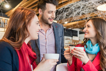 Attractive young woman meeting an old friend while sitting and enjoying a hot drink together with her best friend in a trendy coffee shop