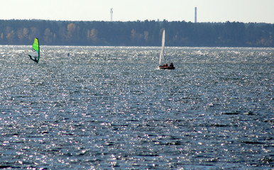 A small sailing yacht with raised sails filled with wind and a windsurfer.