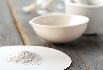 Small ceramic mortar,  bowl  and pestle with white powder on wooden background