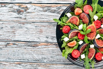 Fresh salad with figs, arugula leaves, cherry tomatoes and feta cheese. Free space for text. Top view.