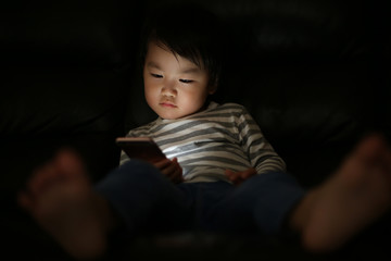 暗い中でスマートフォンを使う男の子