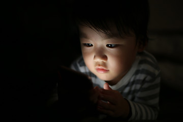 暗い中でスマートフォンを使う男の子