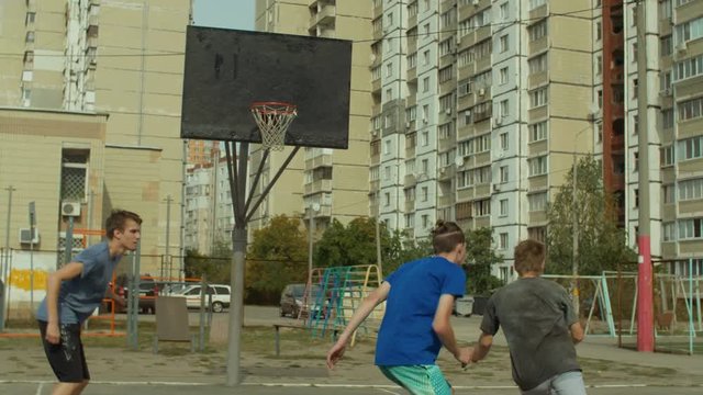 Teenage sporty friends playing streetball game on outdoor court . Basketball player receiving the ball from his teammate and scoring points in paint with layup shot during streetball match outdoors.