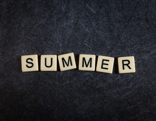 Fototapeta premium Scrabble letter tiles on black slate background spelling Summer