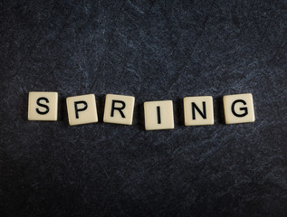 Scrabble letter tiles on black slate background spelling Spring