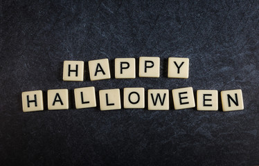 Scrabble letter tiles on black slate background spelling Happy Halloween