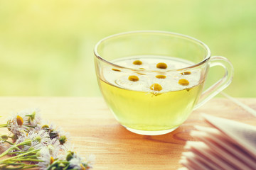 .cup of organic herbal tea with chamomile flowers and open book on wooden table.