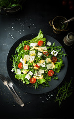 Fresh salad with cherry, arugula, feta, basil and olive oil in a plate