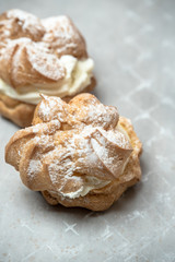 two sweet, sprinkled with powdered sugar cream puffs on a light, stony background