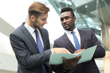 Two multinational young businessmen discussing business at meeting in office.