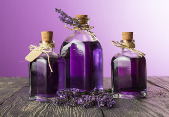 Obraz na płótnie Canvas Three bottles with a fragrant tincture of lavender and fresh twigs on purple background