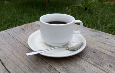 Black coffee in white glass placed on an old wooden table in a green garden.In the morning light sunshine.