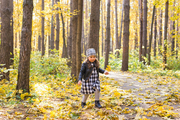 Autumn, seasons and children concept - happy little girl laughing and playing with fallen leaves in park