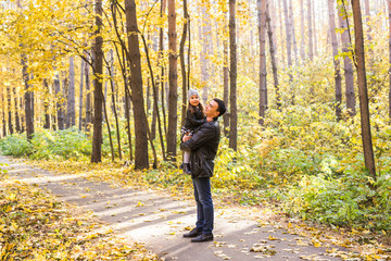 Fototapeta premium Fatherhood, family and leisure concept - father holding little daughter in his arms in autumn park