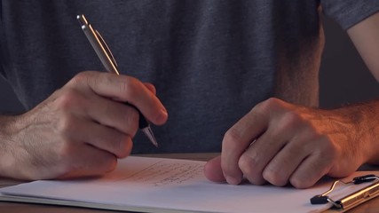 Man making To Do list at home sitting at the desk and writing on clipboard note paper