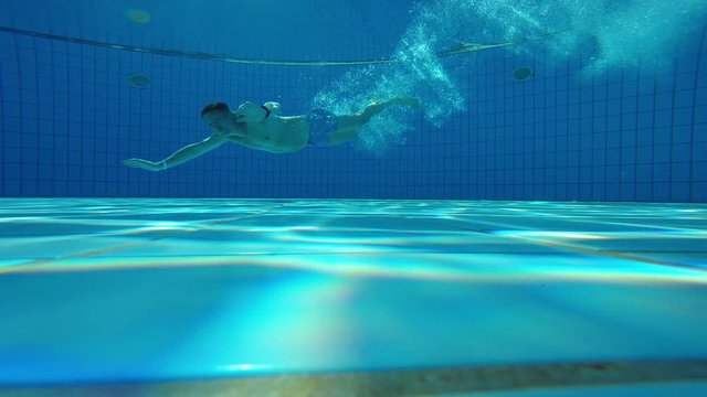 Underwater View Of A Male Jumping And Diving Into Swimming Pool Gesturing Thumb Up At Camera, View From Bottom