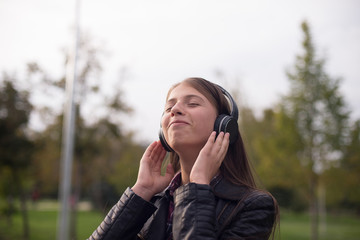 Woman listening to music. Female student girl outside in park listening to music on headphones. Happy young university student of mixed Asian and Caucasian ethnicity.