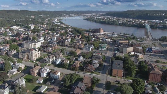 A cinematic orbiting aerial establishing shot of the small rust belt town of Rochester, Pennsylvania, about 25 miles north of Pittsburgh. Bridges over the Ohio River in the distance.  	
