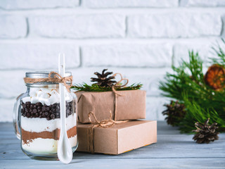 Hot chocolate mix in mason jar and rustic gift boxes on gray table and white brick wall. Christmas and winter holiday budget-friendly gifts idea. Copy space