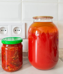 Glass jars with juice and lecho stand on the table