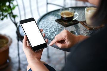 Hand holding smartphone with coffee on the table.