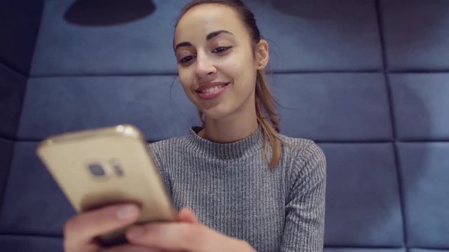 Smartphone girl using app on phone drinking coffee smiling in cafe. Beautiful young casual female professional on mobile phone.