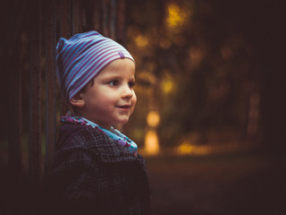 A little girl leaning against a gate in the park. Autumn colors