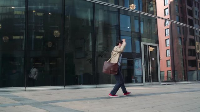 Cheerful man walking and dancing near modern glass building