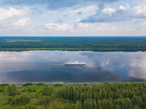 Aerial view of river Volga and cruise ship sailing along. Green riversides and cloudy sky. Summer photo from drone, Russia