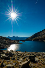 Die Sonne steht am blauen Himmel hoch über einem Bergsee in Österreich