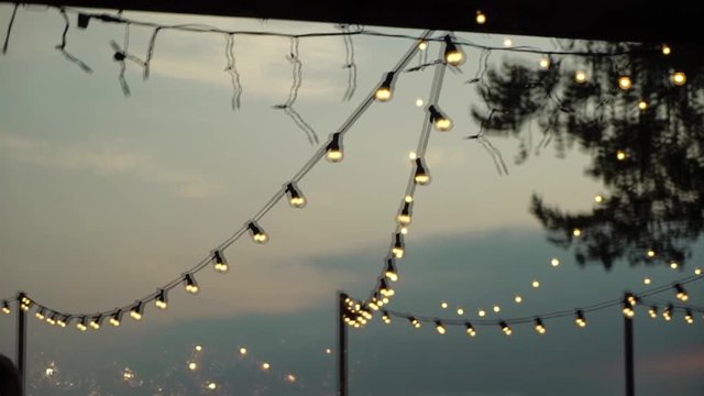 Decorative outdoor string lights hanging in the garden at night or evening time. Decoration at celebration party in forest countryside