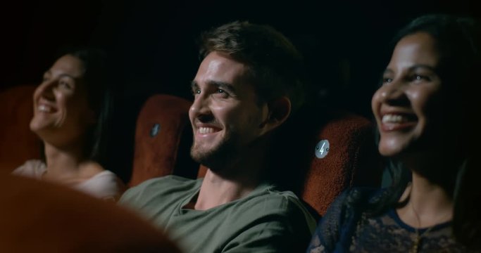 Young man sitting with his friends in a movie theatre laughing and having fun. Slow motion.