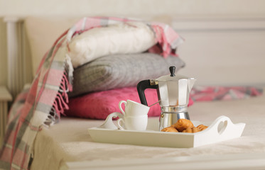 Breakfast in bed. On a white wicker tray there is a coffee maker, coffee cups and croissants.
