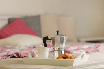 Breakfast in bed. On a white wicker tray there is a coffee maker, coffee cups and croissants.