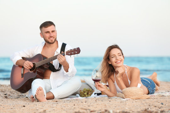 Young couple with guitar having romantic dinner on beach