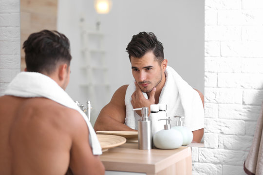 Young Man With Stubble Ready For Shaving Near Mirror In Bathroom