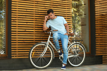 Handsome young hipster man with bicycle near wooden wall outdoors