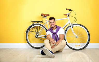 Handsome young hipster man sitting with bicycle near yellow wall