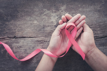 hand holding pink ribbon on wood.  breast cancer awareness. concept healthcare and medicine