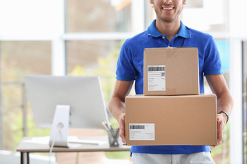 Young courier standing with parcels near office desk. Space for text