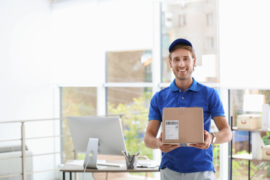 Young courier standing with parcel near office desk. Space for text
