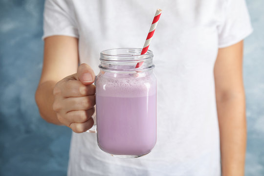 Woman with mason jar of delicious milk shake on color background, closeup