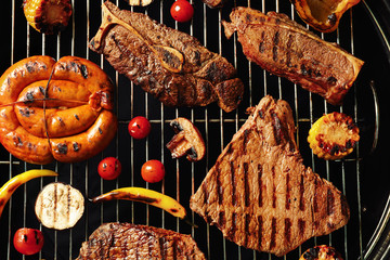 Fresh grilled meat steaks and vegetables on barbecue grate, top view