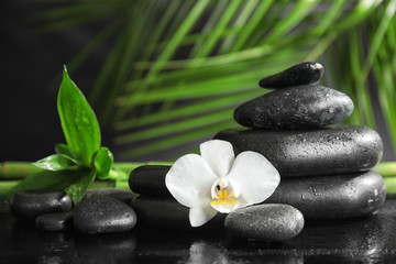 Spa stones with orchid flower and bamboo leaves on dark table