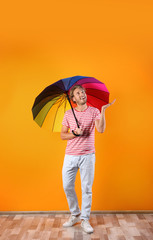 Man with rainbow umbrella near color wall